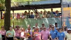 Eine Gruppe Menschen in farbigen T-Shirts und mit bunten Fächern posiert vor einem Paradewagen für ein Gruppenbild.