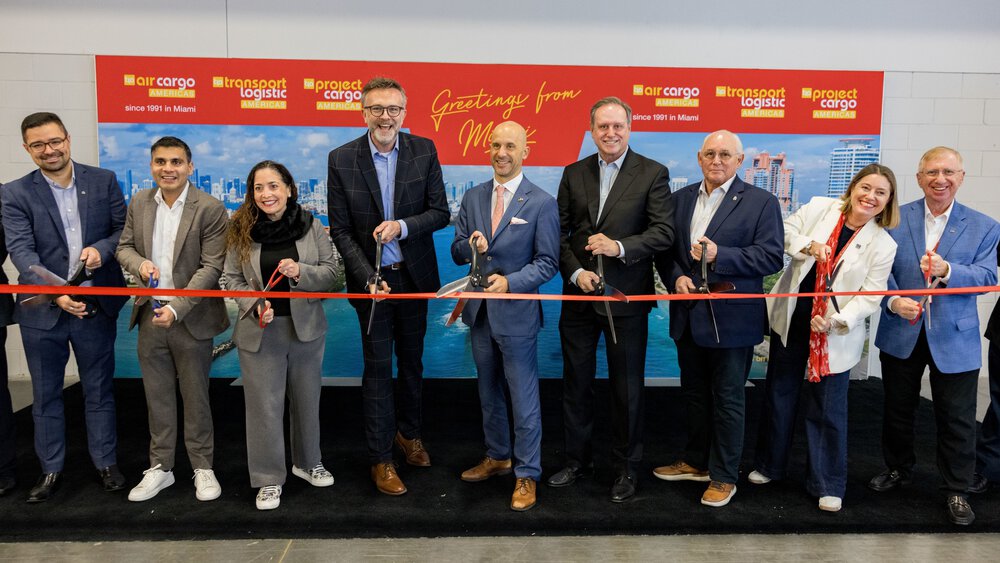 Two women and seven men pose at the opening of the trade fair with large scissors in their hands in front of a long red ribbon that is about to be cut.