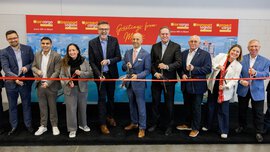 Two women and seven men pose at the opening of the trade fair with large scissors in their hands in front of a long red ribbon that is about to be cut.