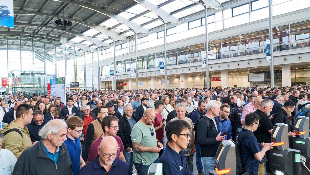 Viele Menschen stehen in einer großen Messehalle und passieren elektronische Zutrittskontrollen