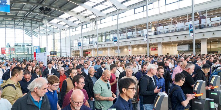 Viele Menschen stehen in einer großen Messehalle und passieren elektronische Zutrittskontrollen