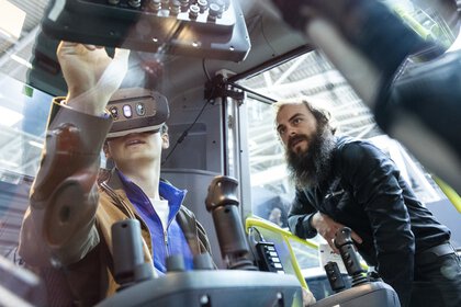 Eine Person testet mit VR-Brille ein Baufahrzeug, während ein Experte daneben steht und das Szenario beobachtet.