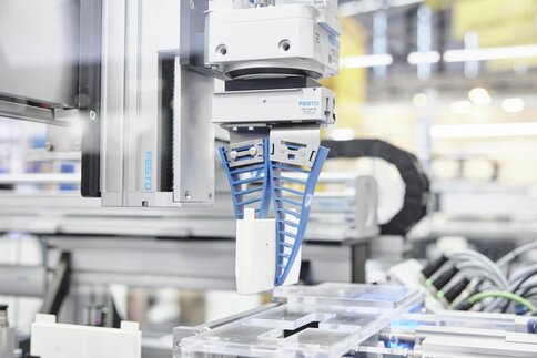 Robotic arm with flexible gripper for handling components in an automated industrial environment with blurred background.