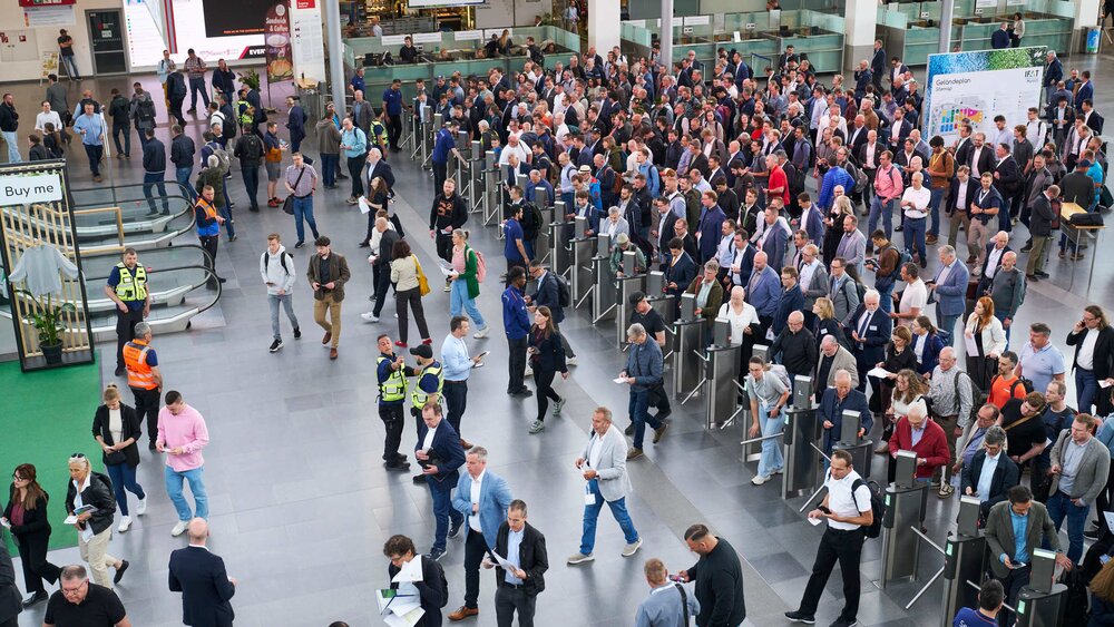 Elevated view of the entrance area of Messe München, with long queues of visitors forming at the entrance turnstiles.