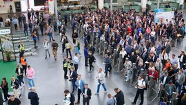 Elevated view of the entrance area of Messe München, with long queues of visitors forming at the entrance turnstiles.