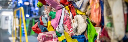 Nahaufnahme eines bunten Haufens komprimierten Plastikmülls vor einer Ballenpressanlage.