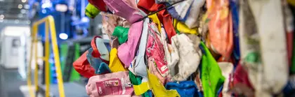 Nahaufnahme eines bunten Haufens komprimierten Plastikmülls vor einer Ballenpressanlage.