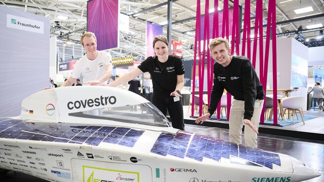 Drei junge Personen präsentieren ein Solarauto am Fraunhofer-Stand auf der Laser World of Photonics 2025 in München.