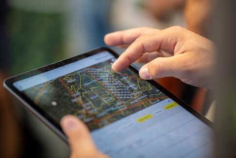 Hand bedient ein Tablet mit digitaler Kartenansicht und markierten Flächen zur Analyse von Wald- oder Geländedaten.