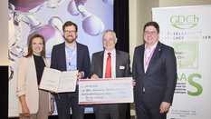 Four people holding a check and laughing into the camera