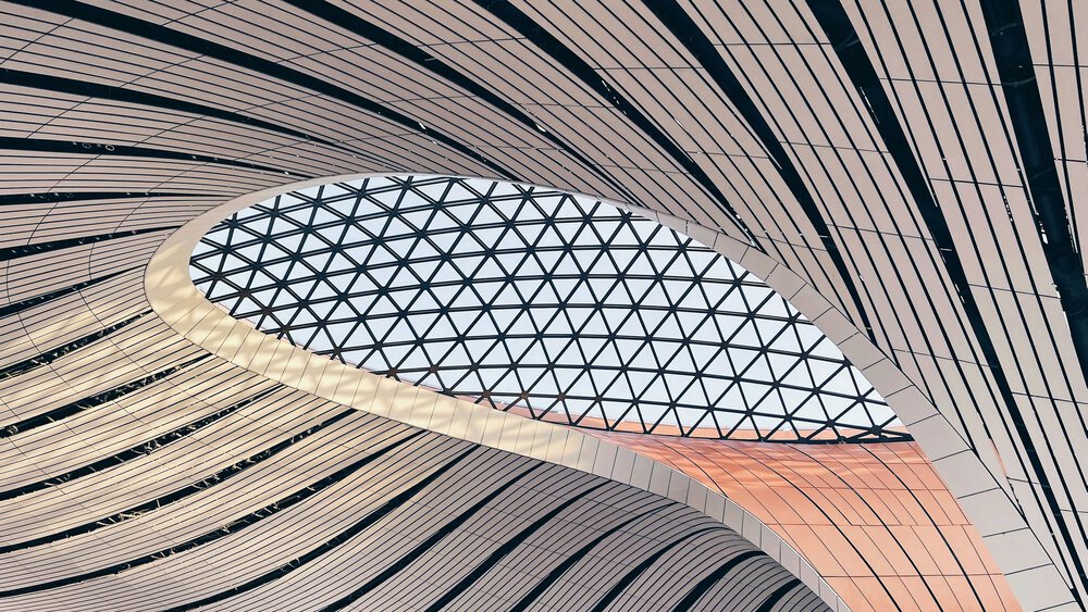 Curved, modern ceiling with striped panels and a large geometric glass skylight in the middle.