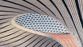 Curved, modern ceiling with striped panels and a large geometric glass skylight in the middle.