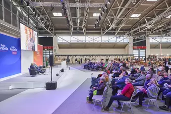 On the left is a stage in a large exhibition hall where two people are giving a talk. On the right is the audience.