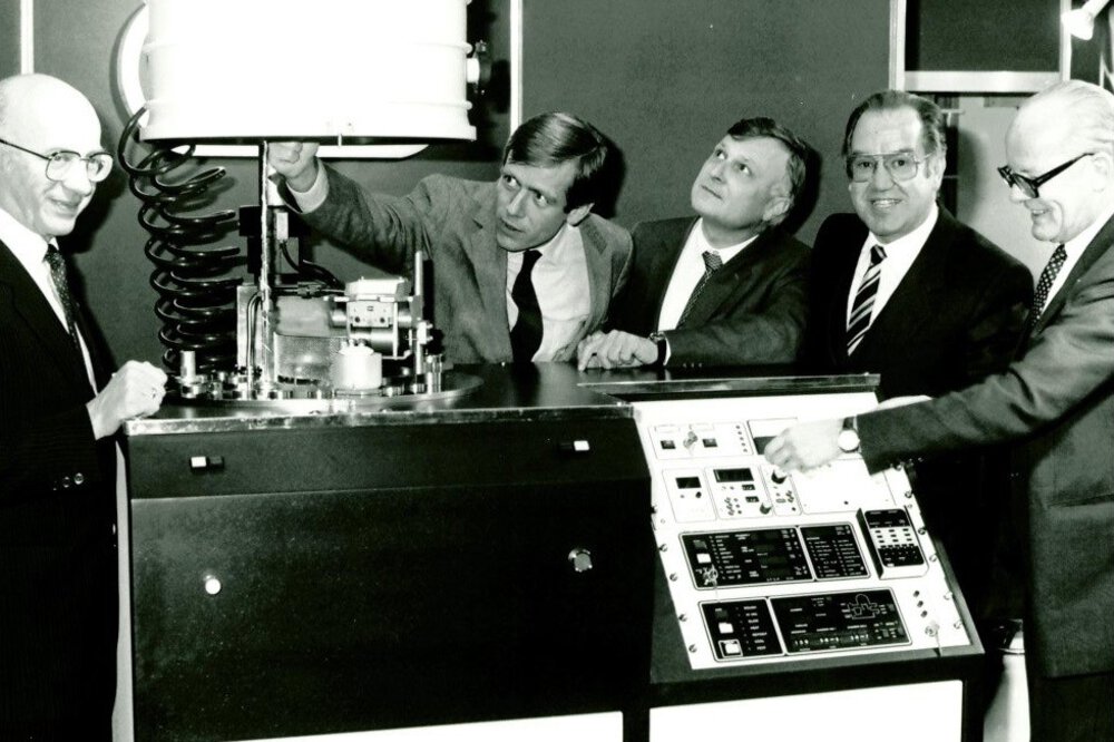 Schwarz-weißes Foto von einer früheren productronica. Mehrere Männer in Anzügen stehen um eine Maschine herum, drücken Knöpfe und schauen interessiert.