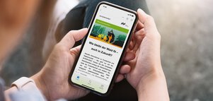 Eine Person hält ein Smartphone, auf dem Besucherinformationen der INTERFORST zu sehen sind, mit dem Titel 