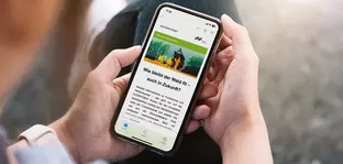 Eine Person hält ein Smartphone, auf dem die Webseite der INTERFORST-Messe in deutscher Sprache zu sehen ist.