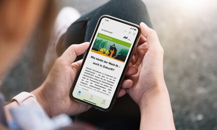 One person holds a smartphone on which visitor information from INTERFORST can be seen with the title 