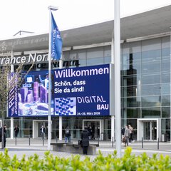 Eingang Kölnmesse mit einem großen Display an der Außenfassade, auf der die digitalBAU ihre Besucher willkommen heißt.