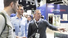 Drei Männer stehen an einem Stand auf der digitalBAU und betrachten etwas außerhalb des Bildes. Im Hintergrund sind weitere Stände zu sehen.