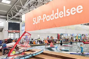 Indoor-Wasserbecken auf der Messe f.re.e mit Kindern und Erwachsenen beim Stand-Up-Paddling unter einem großen „SUP-Paddelsee“-Banner.