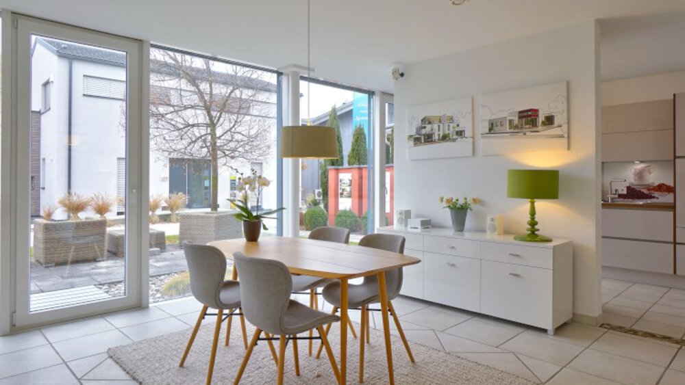 Moderner Essbereich mit Tisch, grauen Stühlen, Hängelampe und Glastüren mit Blick auf eine Terrasse.