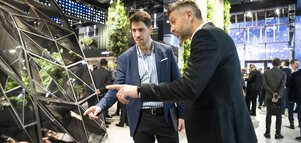 Two men in business attire talk about a window construction made up of triangular panes.