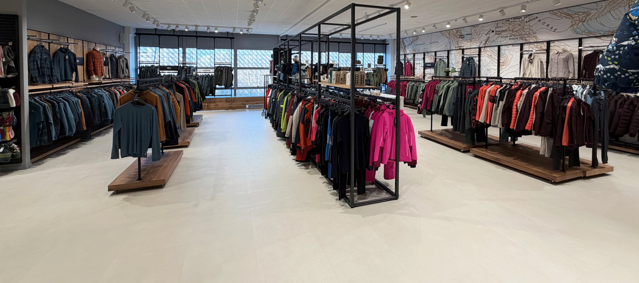 Ein Bekleidungsgeschäft mit Regalen mit Jacken, Mänteln und Hemden, die unter heller Beleuchtung ordentlich angeordnet sind.