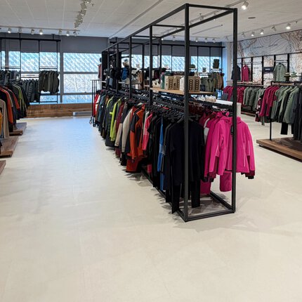 Ein Bekleidungsgeschäft mit Regalen mit Jacken, Mänteln und Hemden, die unter heller Beleuchtung ordentlich angeordnet sind.