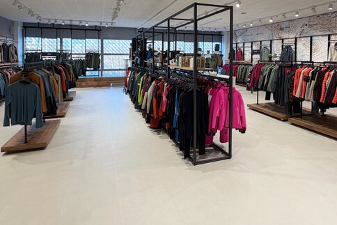 Ein Bekleidungsgeschäft mit Regalen mit Jacken, Mänteln und Hemden, die unter heller Beleuchtung ordentlich angeordnet sind.