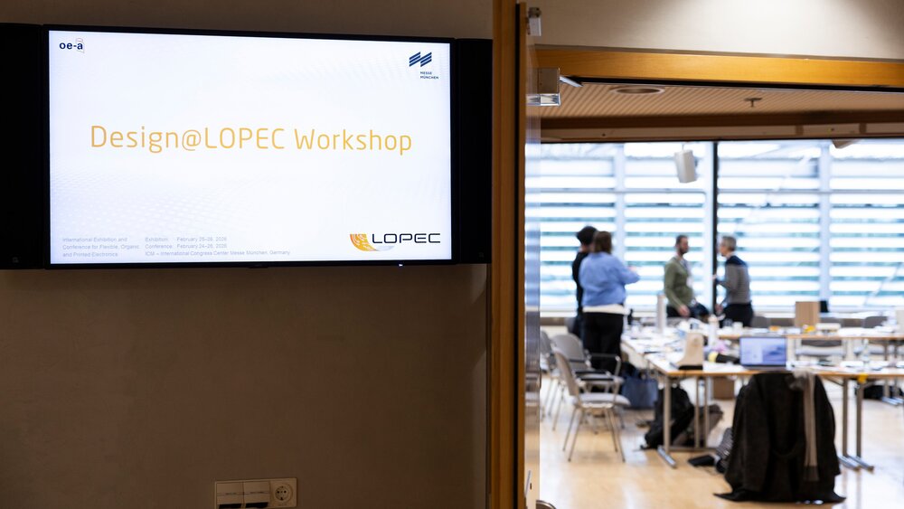 Screen displaying Design@LOPEC Workshop sign with view into a workshop room and participants