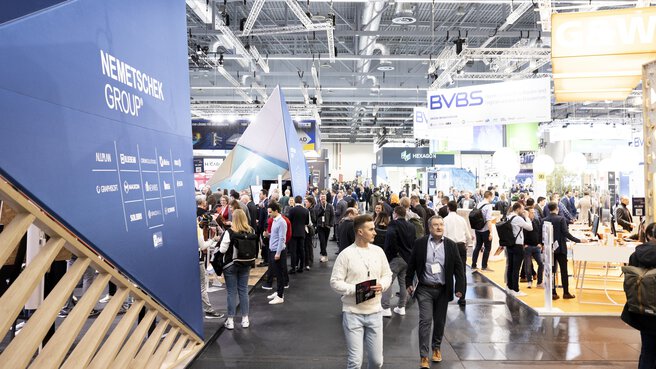 Menschenmenge zwischen verschiedenen Messeständen und Ausstellungen in einer großen Messehalle.