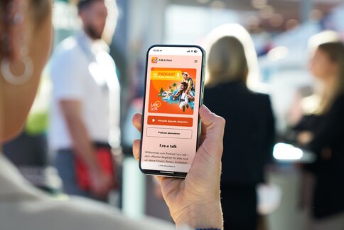 Eine Person schaut auf das Handy Display, auf dem der free Podcast zu sehen ist