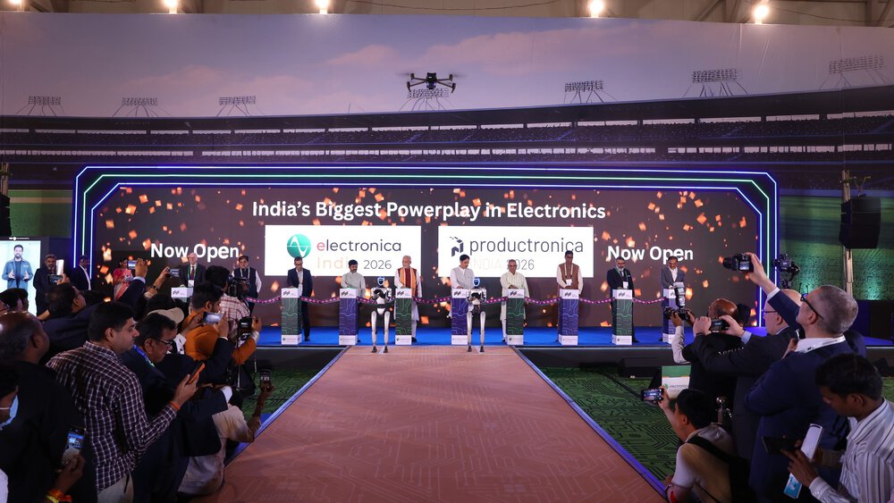 A group of people on stage at the opening ceremony of an electronics trade show, with media and audience members taking photos.