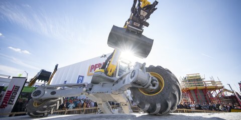 All-terrain construction machine with shovel during a live demonstration on the open-air site.