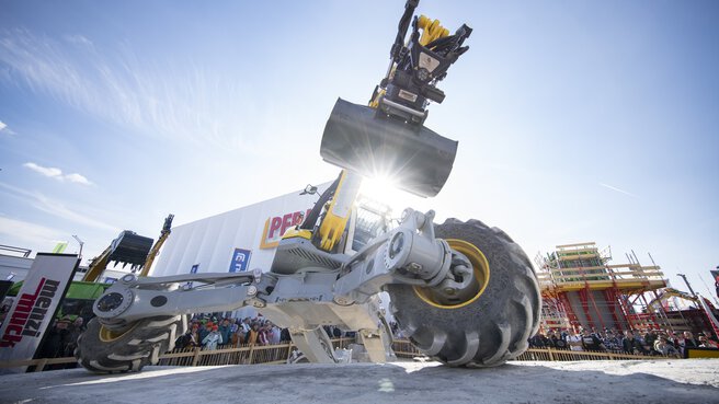 All-terrain construction machine with shovel during a live demonstration on the open-air site.