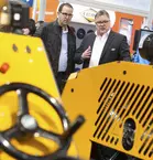 Two men inspect a large yellow industrial machine at bauma.