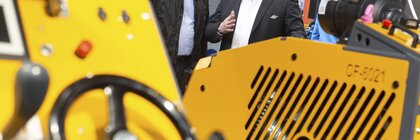 Two men inspect a large yellow industrial machine at bauma.