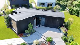 Ein modernes, schwarzes, einstöckiges Haus mit kantigem Design, großen Fenstern und einem begrünten Hof.