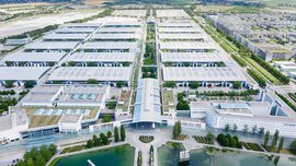 Ein Blick aus der Vogelperspektive über das gesamte Gelände der Messe München mit dem Messesee im Vordergrund, den zahlreichen Hallen und Feldern im Hintergrund.