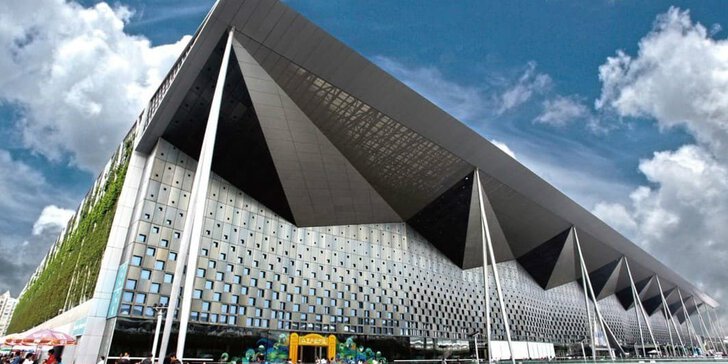 A large, modern building with angular architecture under a partly cloudy sky, in front of which people have gathered.