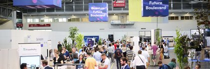 Messehalle mit vielen Besucherinnen und Besuchern an Ständen und Sitzbereichen, über ihnen hängen große Displays mit der Aufschrift „Quantum Future Boulevard“.