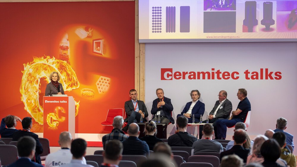 Fünf Männer in Anzügen sitzen auf einer Bühne der ceramitec talks und sprechen zu einem interessierten Publikum. Eine Frau moderiert den Talk.