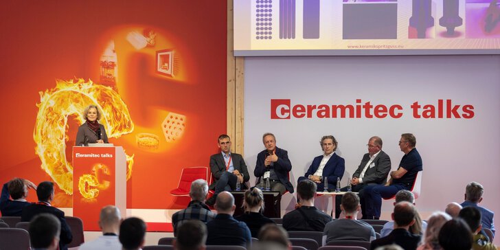 Fünf Männer in Anzügen sitzen auf einer Bühne der ceramitec talks und sprechen zu einem interessierten Publikum. Eine Frau moderiert den Talk.