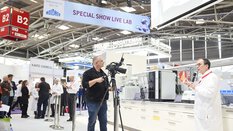 ein Mann in Jeans filmt eine Person in einem Laborkittel dabei, wie sie etwas erklärt