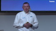 Eine Person im weißen CDE-Shirt steht vor einem Bildschirm und faltet die Hände.