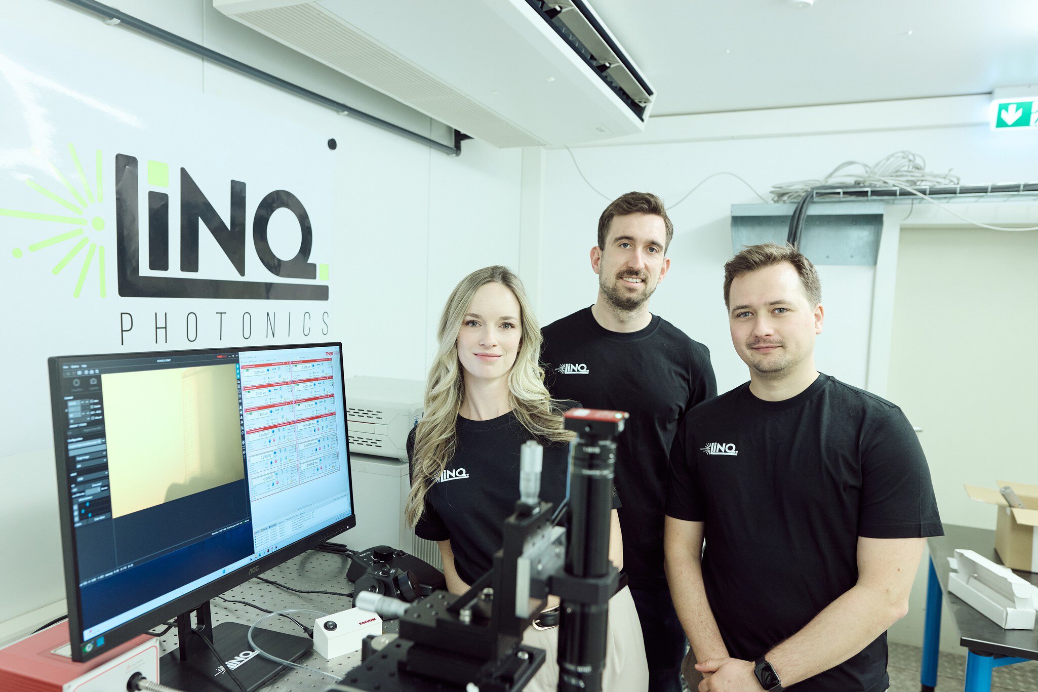 Drei Mitarbeitende von LINQ Photonics stehen in einem modernen Labor neben einem Monitor und optischen Messgeräten. Im Hintergrund ist das Firmenlogo an der Wand zu sehen.