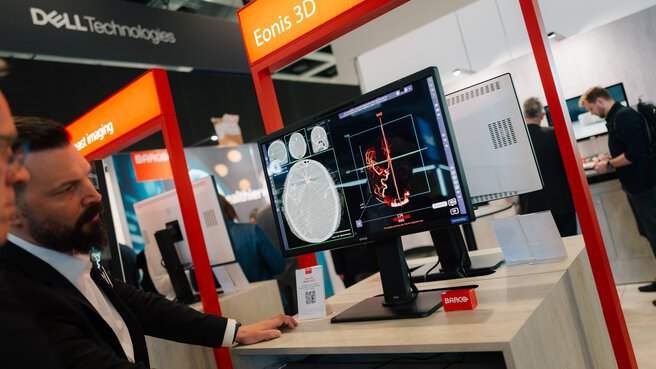 Medical 3D imaging displayed on a monitor at a DMEA booth with professionals in the foreground