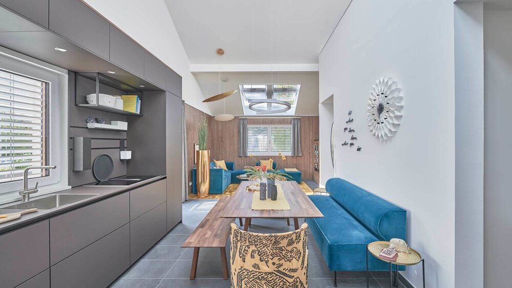 Moderner Essbereich mit Holztisch, blau gepolsterter Bank und Blick in ein stilvolles Wohnzimmer.