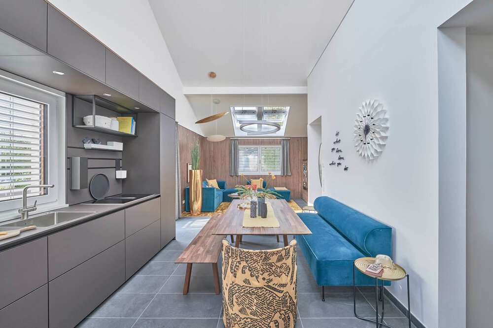 Moderner Essbereich mit Holztisch, blau gepolsterter Bank und Blick in ein stilvolles Wohnzimmer.