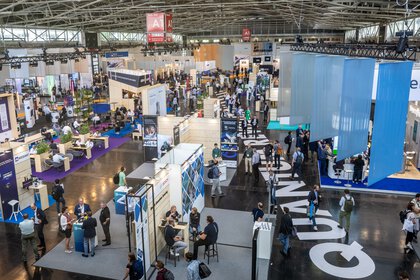 Vogelperspektive auf die Halle A1 der World of Quantum, mit vielen modernen Messeständen und Besuchern.